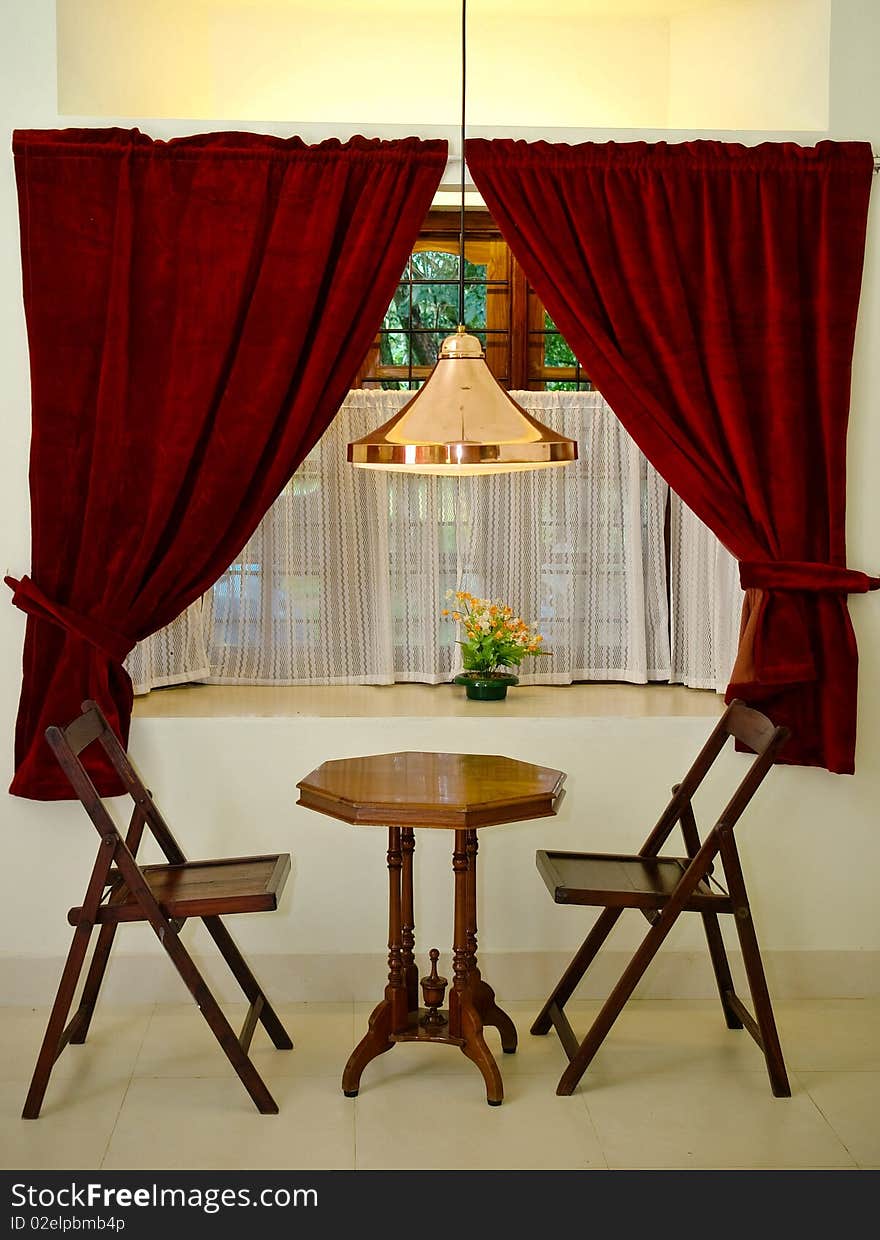 A beautifully lit window overlooking antique wooden chairs and table. An overhead reading lamp. A beautifully lit window overlooking antique wooden chairs and table. An overhead reading lamp.