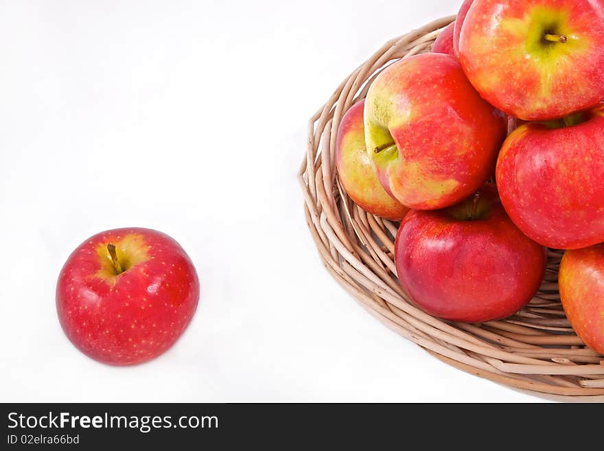 Red apples on a basket and one rolled away on white backround