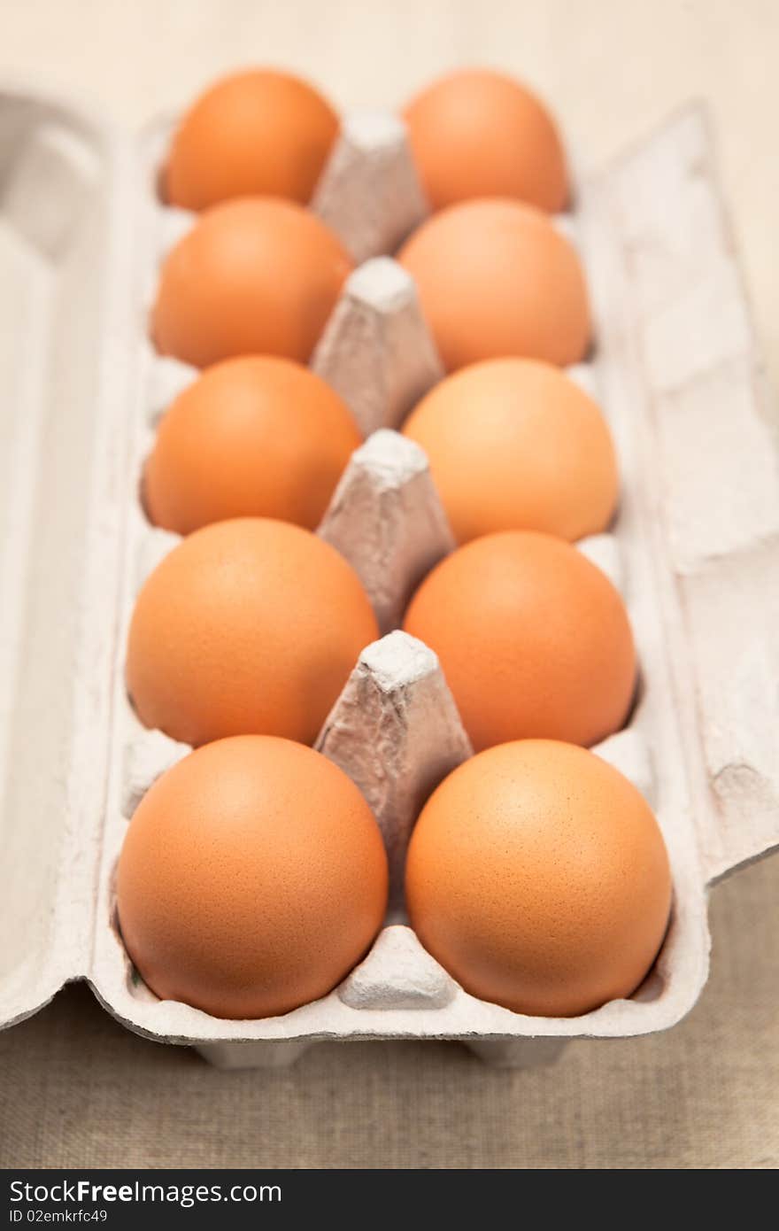 Open cardboard eggbox with ten brown eggs. Shallow dof, focus is on front eggs. Open cardboard eggbox with ten brown eggs. Shallow dof, focus is on front eggs.