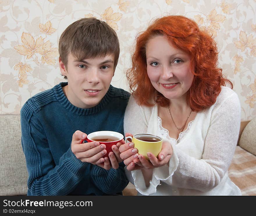 Smiling woman and teen boy have tea on sofa at home. Smiling woman and teen boy have tea on sofa at home