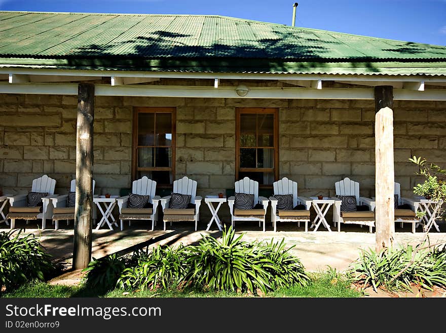 Perspective shot of many white wooden chairs on veranda of old stone building in shade to rest and relax. Perspective shot of many white wooden chairs on veranda of old stone building in shade to rest and relax