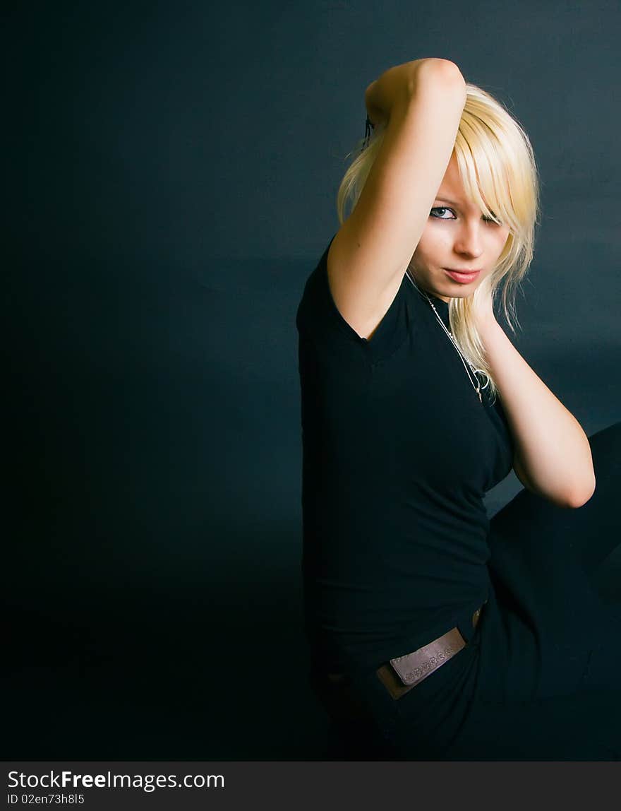 Portrait of a beautiful black dressed blonde, she is sitting in a studio with her arms touching her head. Portrait of a beautiful black dressed blonde, she is sitting in a studio with her arms touching her head