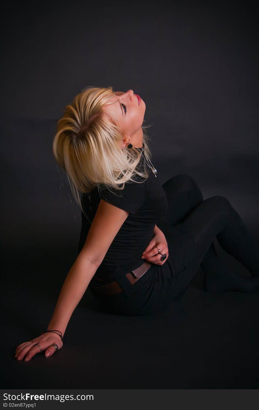 Portrait of a beautiful black dressed blonde in a studio, she is sitting and throwing back her head. Portrait of a beautiful black dressed blonde in a studio, she is sitting and throwing back her head