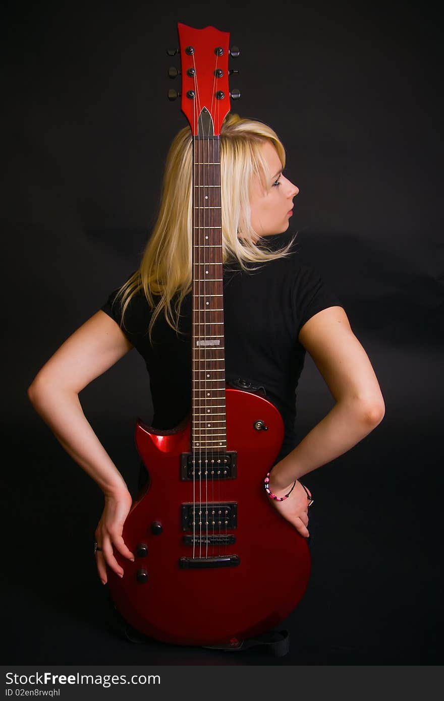 Beautiful slim blonde in black dress holding a red guitar. Beautiful slim blonde in black dress holding a red guitar