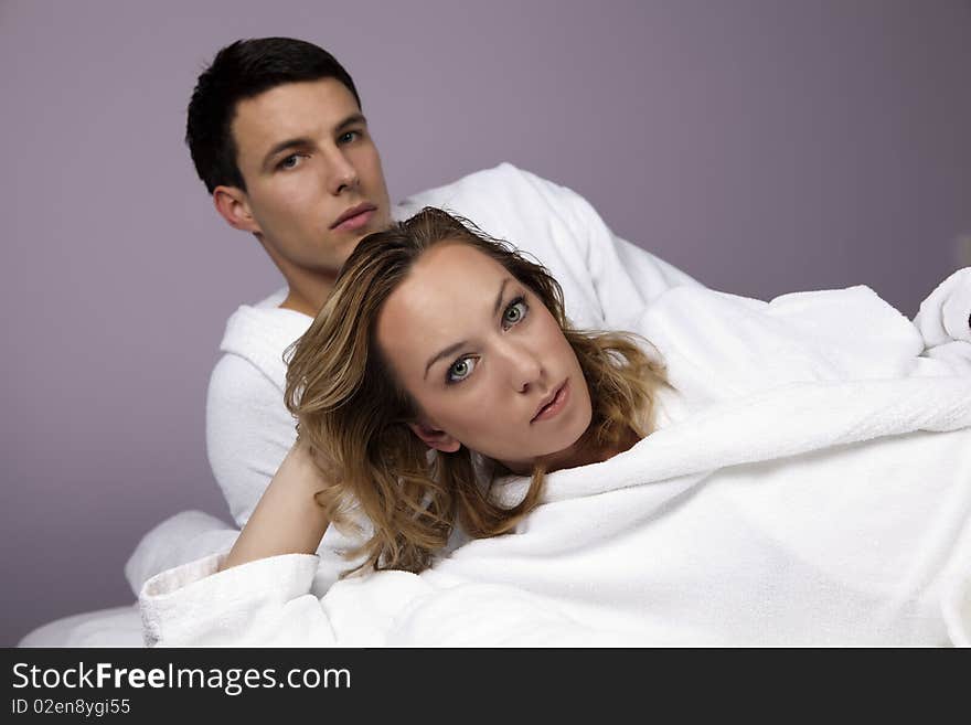 Young handsome couple looking at the camera, lying on the massage table in the spa, wearing white towel robes. Young handsome couple looking at the camera, lying on the massage table in the spa, wearing white towel robes.