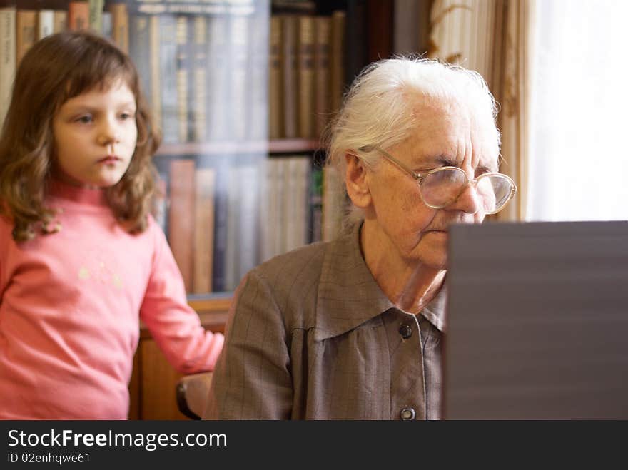 Great-grandmother working with laptop and granddoughter  standing behind. Great-grandmother working with laptop and granddoughter  standing behind