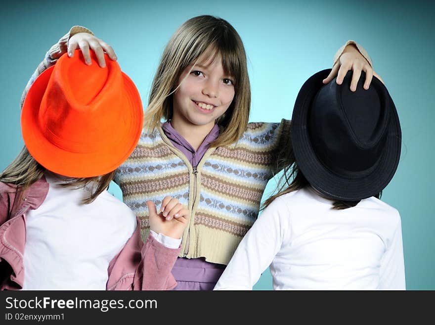 Three white children playing with black and orange hat, turquoise background. Three white children playing with black and orange hat, turquoise background