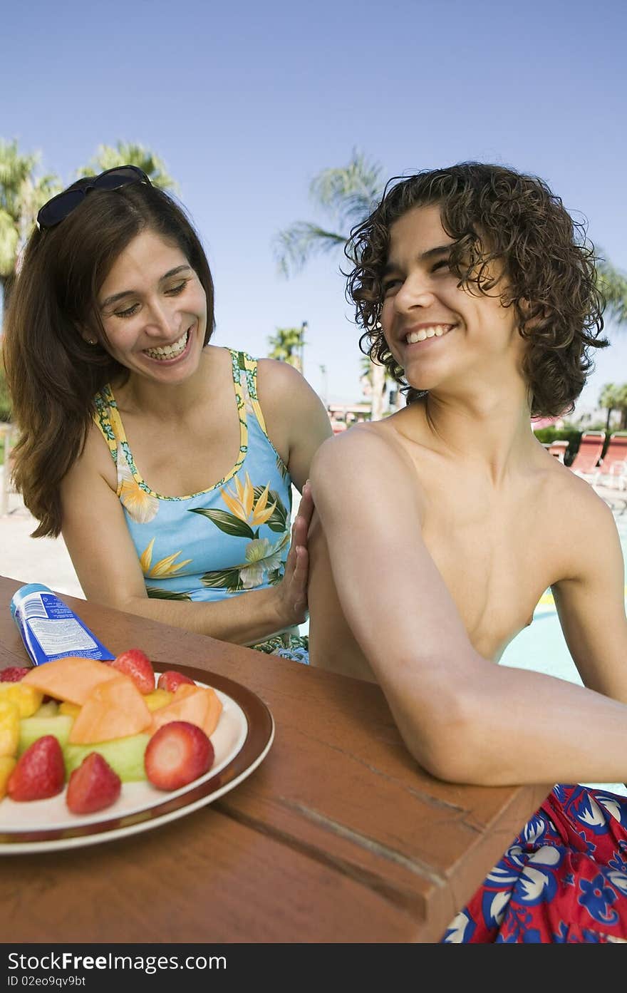 Woman applying sunscreen to son (13-15) at swimming pool.