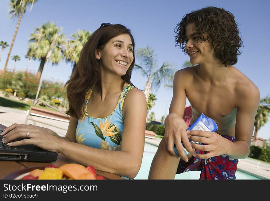 Mother and son (13-15) at swimming pool, mother using laptop. Mother and son (13-15) at swimming pool, mother using laptop.