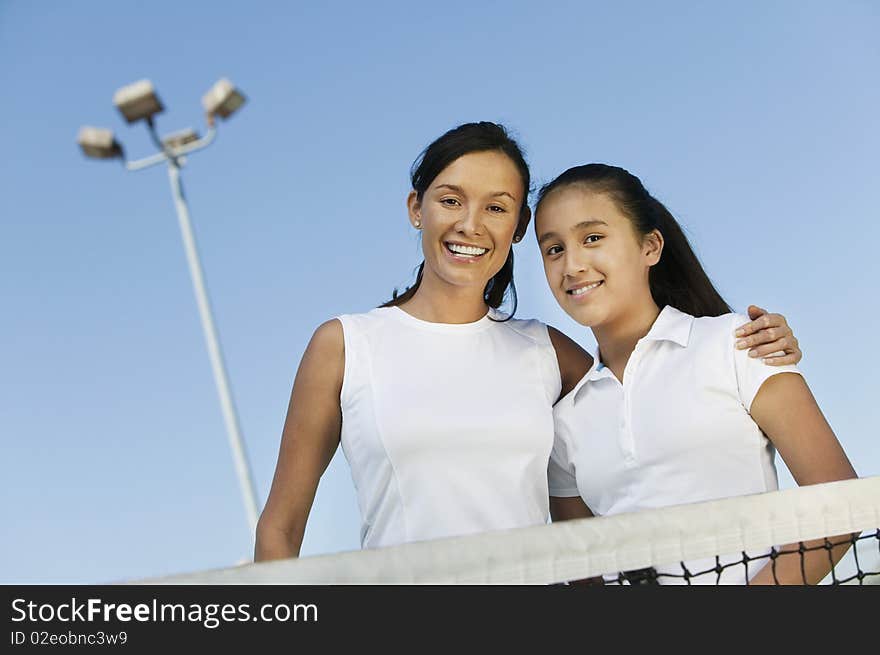 Mother and daughter standing at net on tennis court, portrait, low angle view. Mother and daughter standing at net on tennis court, portrait, low angle view