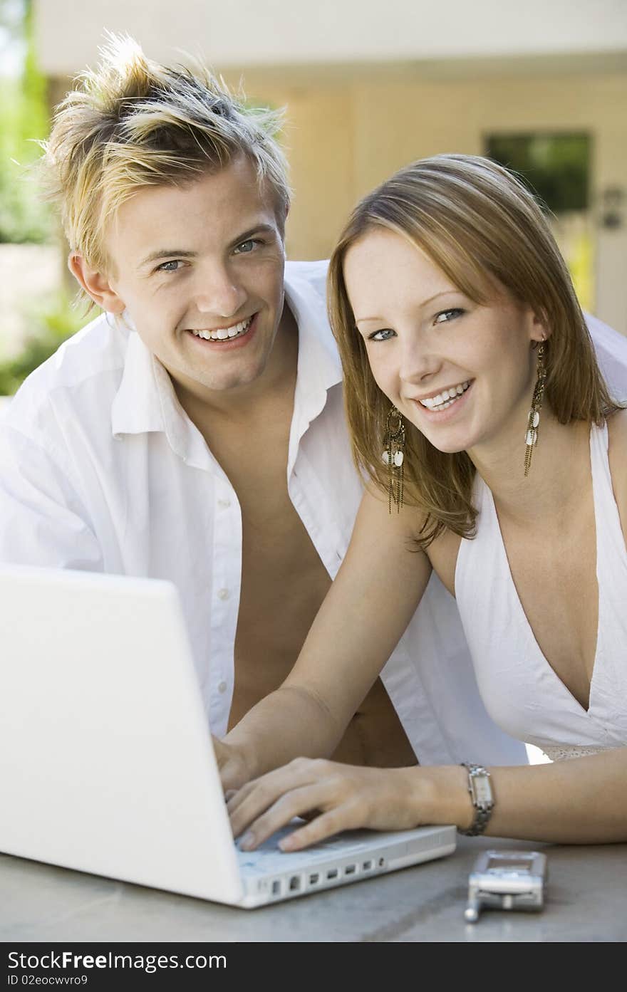 Couple Sitting At Backyard Table Using Laptop