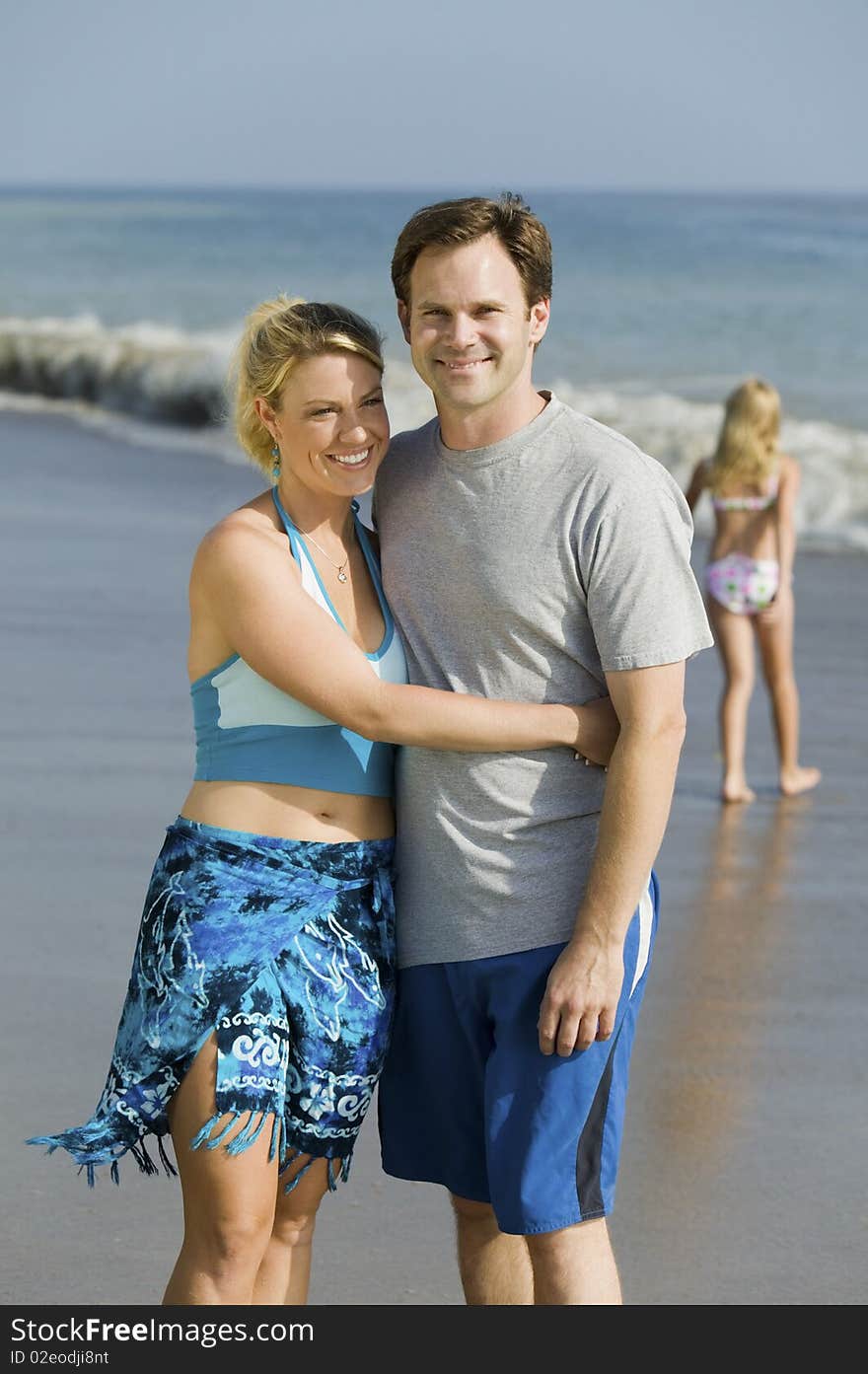 Couple embracing on Beach, daughter n background. Couple embracing on Beach, daughter n background