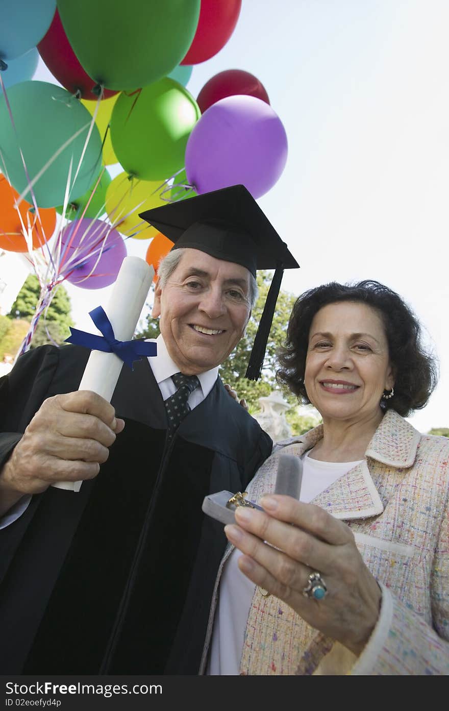 Senior graduate receiving present from wife outside, low angle view