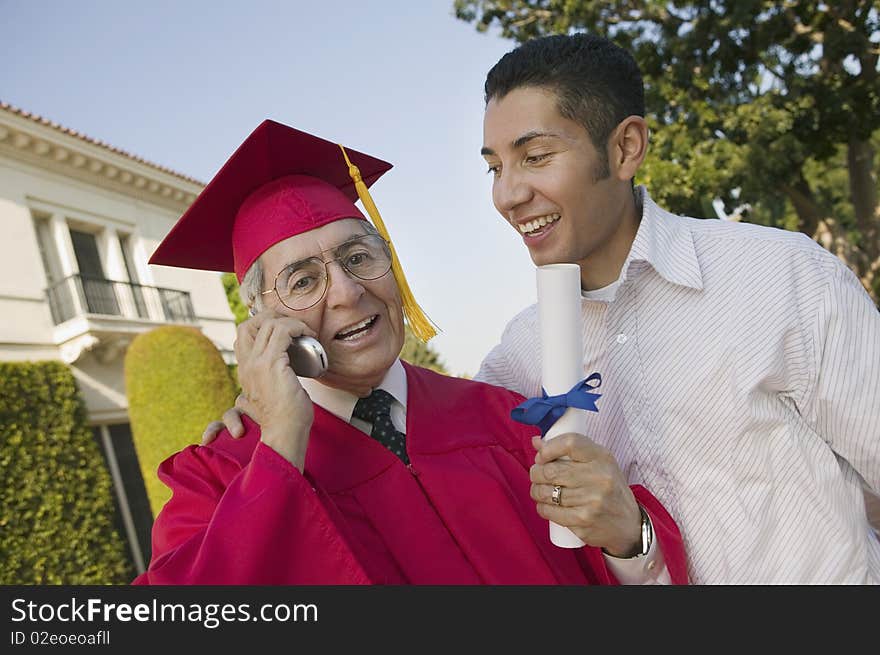 Senior Graduate using cell phone outside with son, low angle view