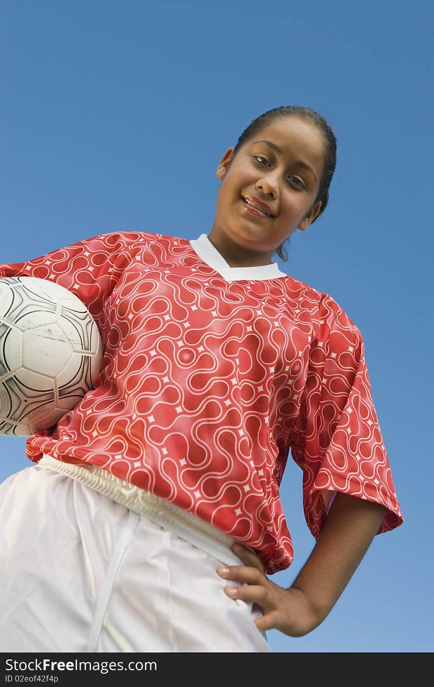 Girl (13-17) in soccer kit holding ball, portrait, low angle view