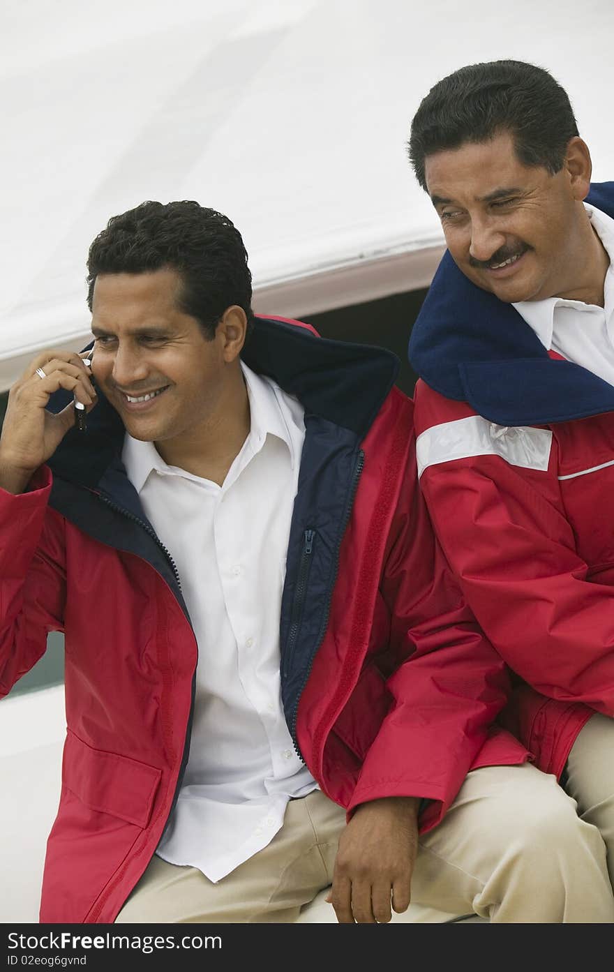 Two men relaxing on yacht, one man using mobile phone