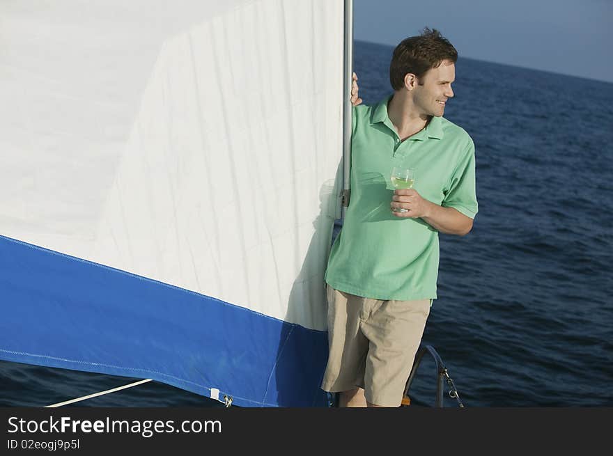 Man standing on sailboat, holding glass of white wine. Man standing on sailboat, holding glass of white wine