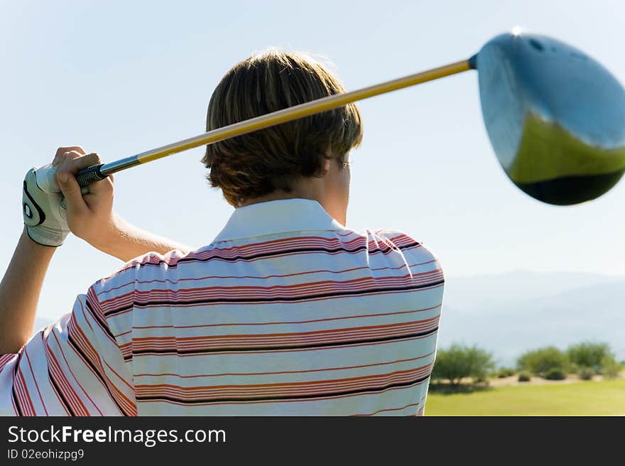 Golfer swinging club, back view