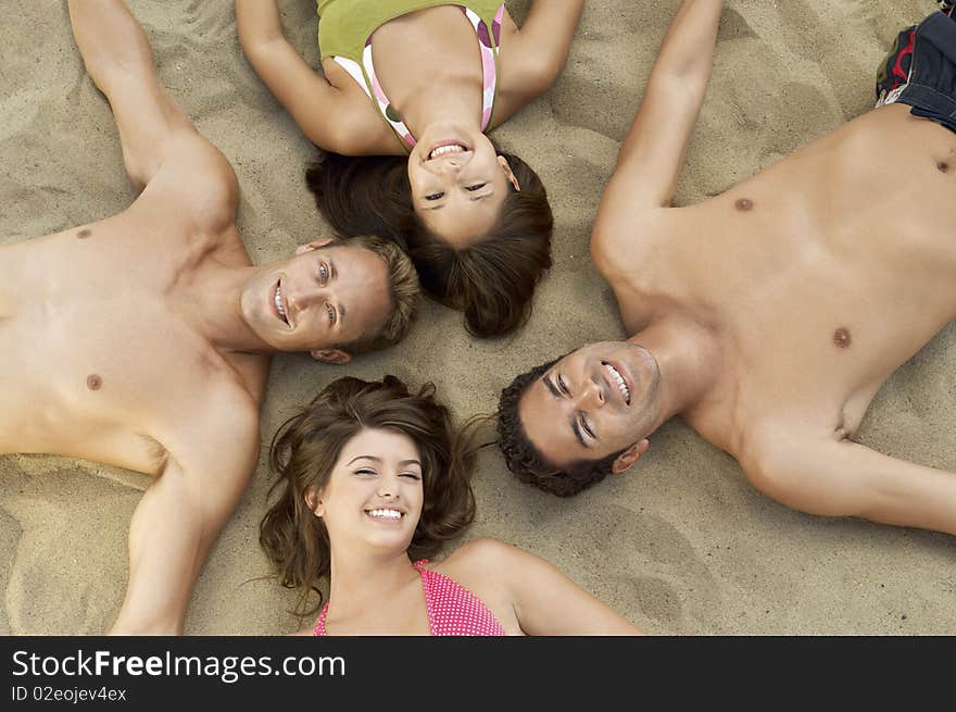 Four young adults lying down in circle on sand, smiling, portrait, view from above