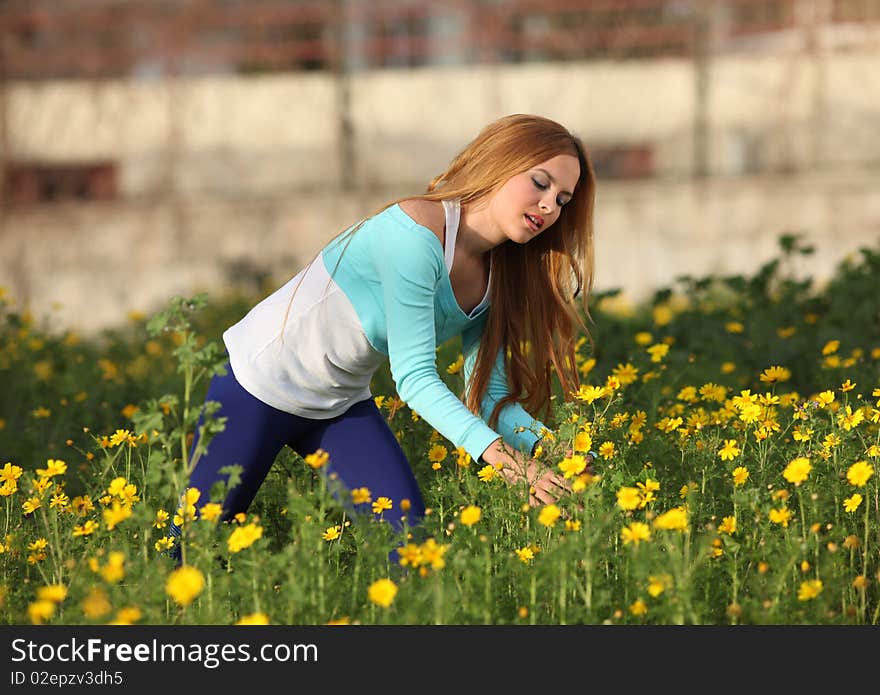 Beautiful young blonde woman standing in blooming meadow in spring, yellow flowers in hand; shallow depth of field. Beautiful young blonde woman standing in blooming meadow in spring, yellow flowers in hand; shallow depth of field