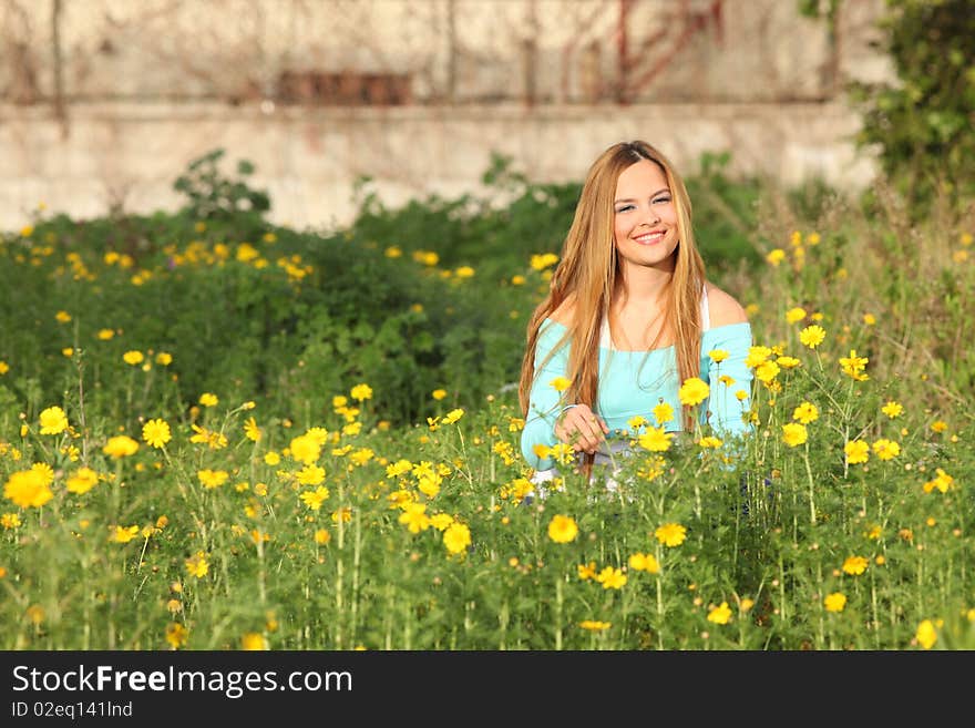 Beautiful young blonde woman sitting in blooming meadow in spring, smiling; shallow depth of field. Beautiful young blonde woman sitting in blooming meadow in spring, smiling; shallow depth of field