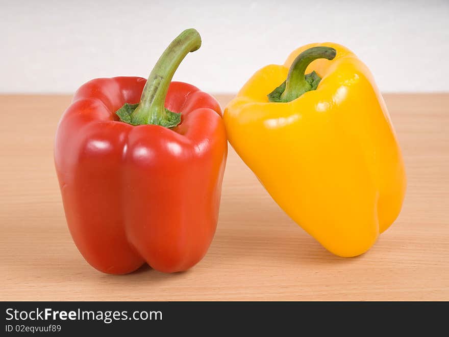 These are two red and yellow peppers are on the kitchen table. These are two red and yellow peppers are on the kitchen table