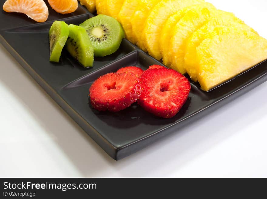 Sliced of ananas, kiwi, mandarin and strawberries on a black saucer. Sliced of ananas, kiwi, mandarin and strawberries on a black saucer