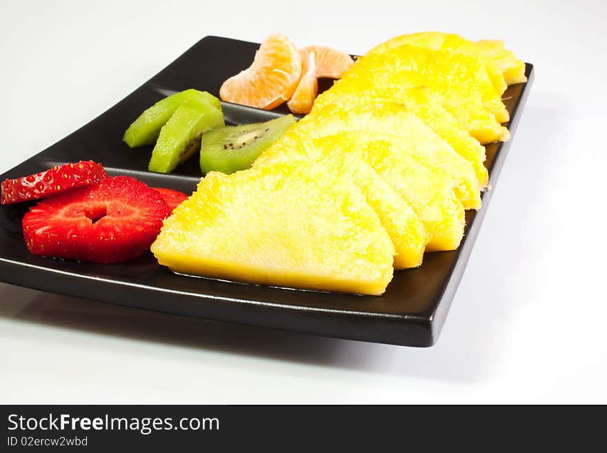 Sliced of ananas, kiwi, mandarin and strawberries on a black saucer. Sliced of ananas, kiwi, mandarin and strawberries on a black saucer