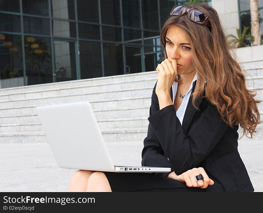 Business woman sitting on the steps with notebooks and monitors the exchange