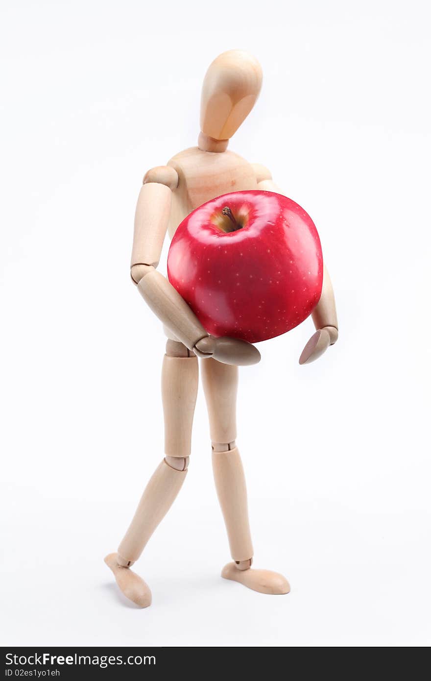 Wooden man holding a large red apple. Isolated over white