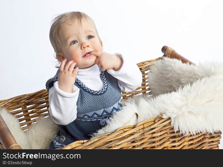 Nice little girl sitting in a wicker basket covered with fell isolated on white background. Nice little girl sitting in a wicker basket covered with fell isolated on white background