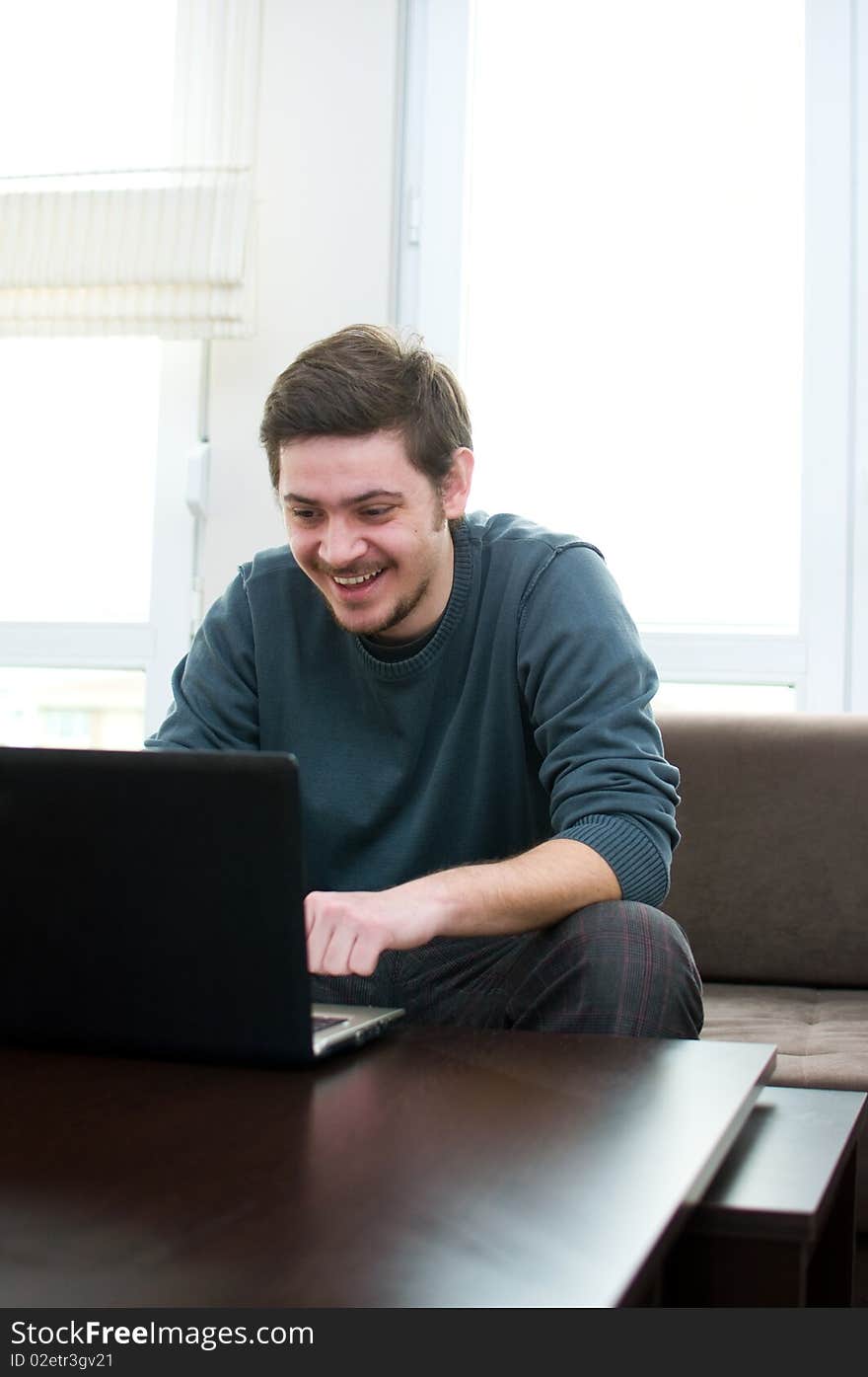 Portrait of a smiling man working on a laptop at home sitting on the couch. Portrait of a smiling man working on a laptop at home sitting on the couch