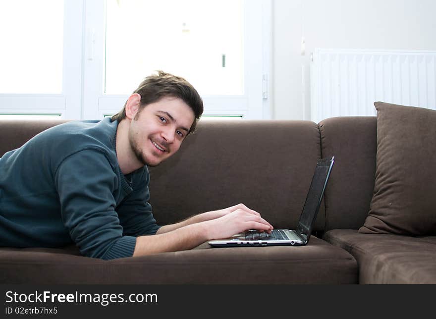 Portrait of a smiling man working on a laptop at home sitting on the couch. Portrait of a smiling man working on a laptop at home sitting on the couch