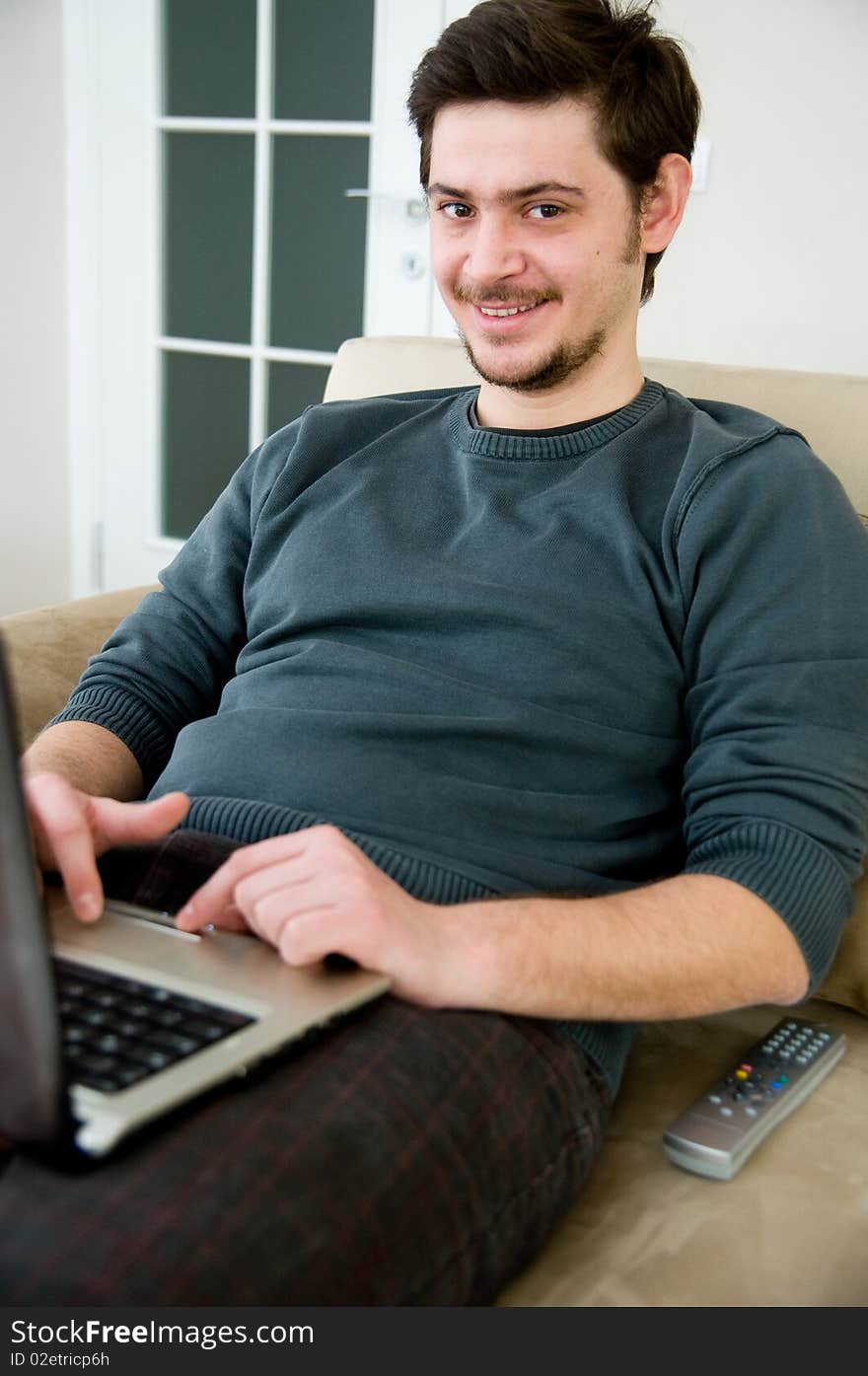 Portrait of a smiling man working on a laptop at home sitting on the couch. Portrait of a smiling man working on a laptop at home sitting on the couch