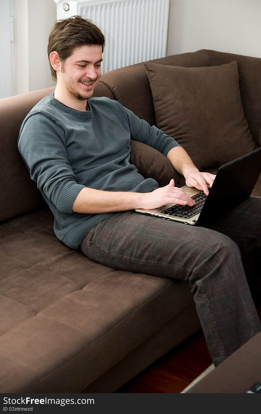 Portrait of a smiling man working on a laptop at home sitting on the couch. Portrait of a smiling man working on a laptop at home sitting on the couch