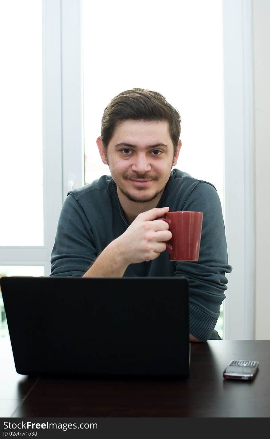 Portrait of a man working on a laptop at home drinking coffee. Portrait of a man working on a laptop at home drinking coffee