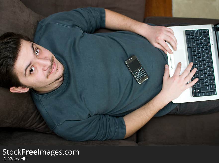 Portrait of a smiling man working on a laptop at home sitting on the couch. Portrait of a smiling man working on a laptop at home sitting on the couch