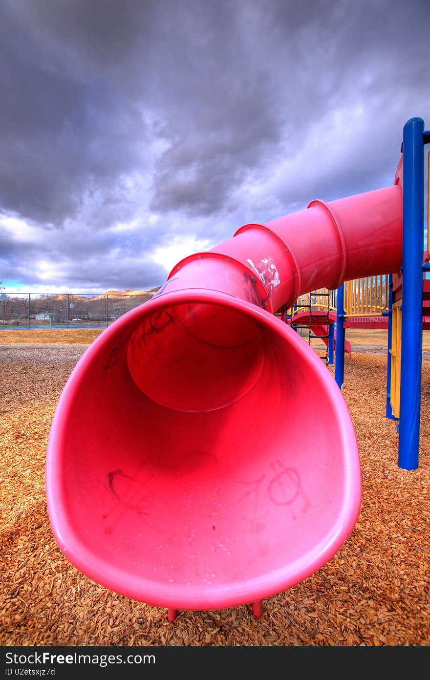 A child's playground set tube slide with wood-chips about on the ground.