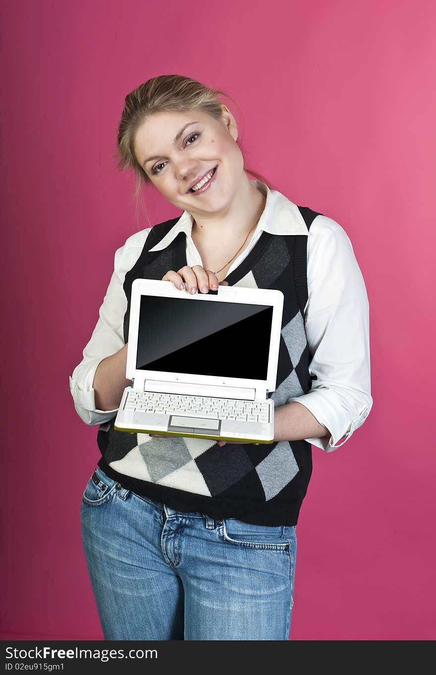 Blond young woman with laptop posing on pink background, studio shot