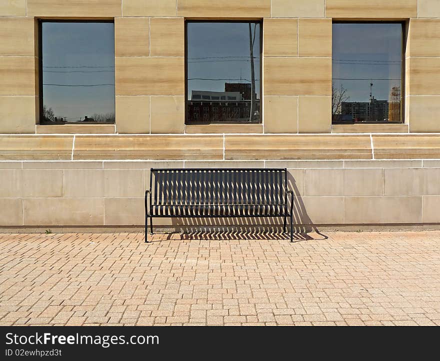 Image of a public bench under three windows on an interlocking brick surface. Image of a public bench under three windows on an interlocking brick surface