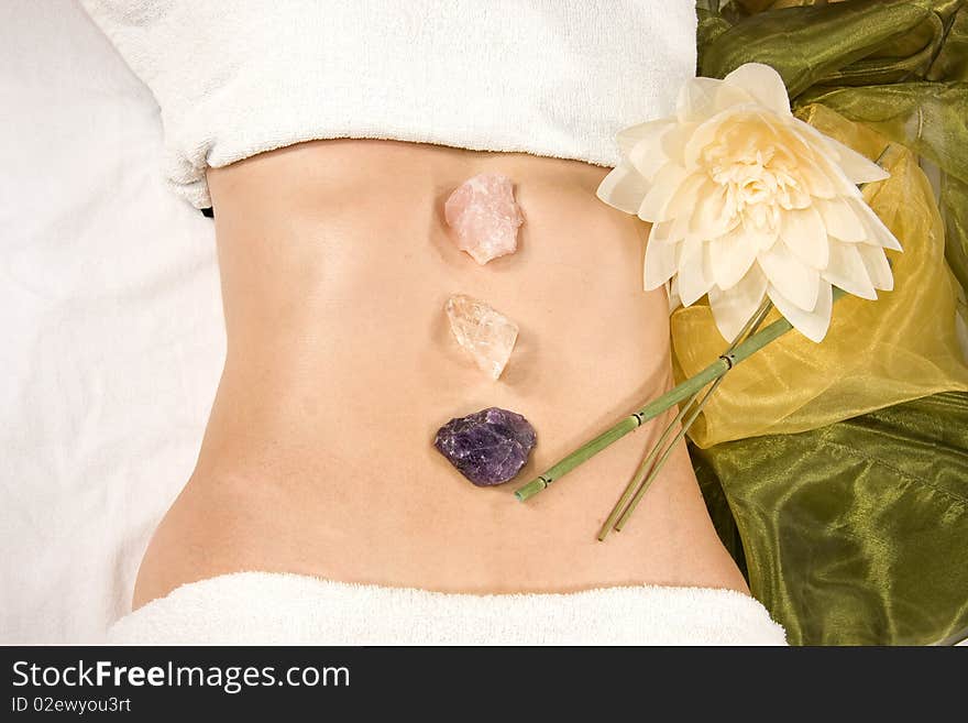 A wellness composition showing the abdomen of a natural mature woman, stones, a flower and a silk scarf