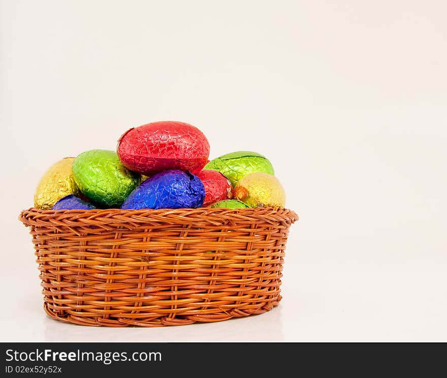 Colorful easter eggs wrapped in shiny foil in wicker basket white background. Colorful easter eggs wrapped in shiny foil in wicker basket white background