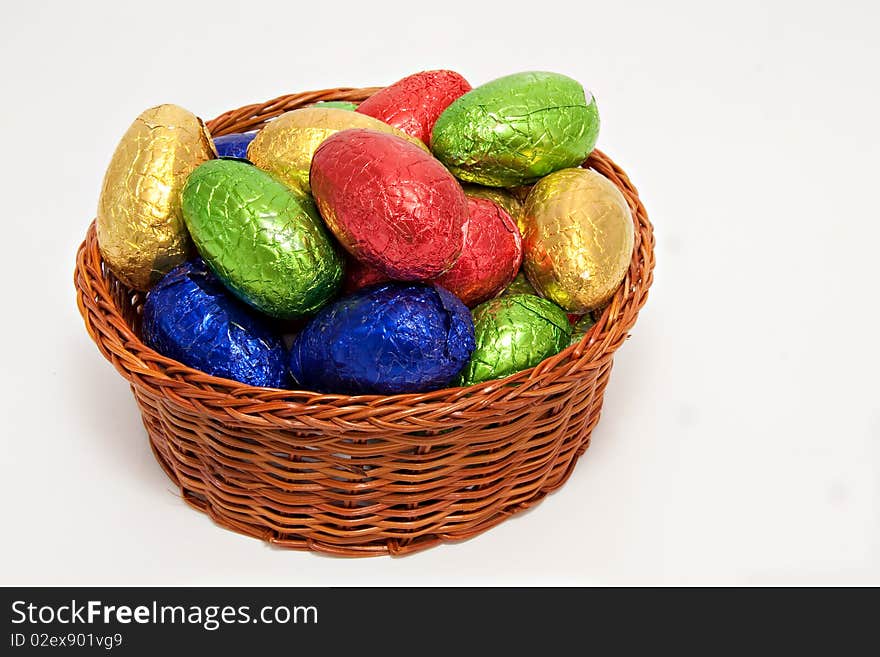 Colorful easter eggs wrapped in shiny foil in wicker basket white background. Colorful easter eggs wrapped in shiny foil in wicker basket white background