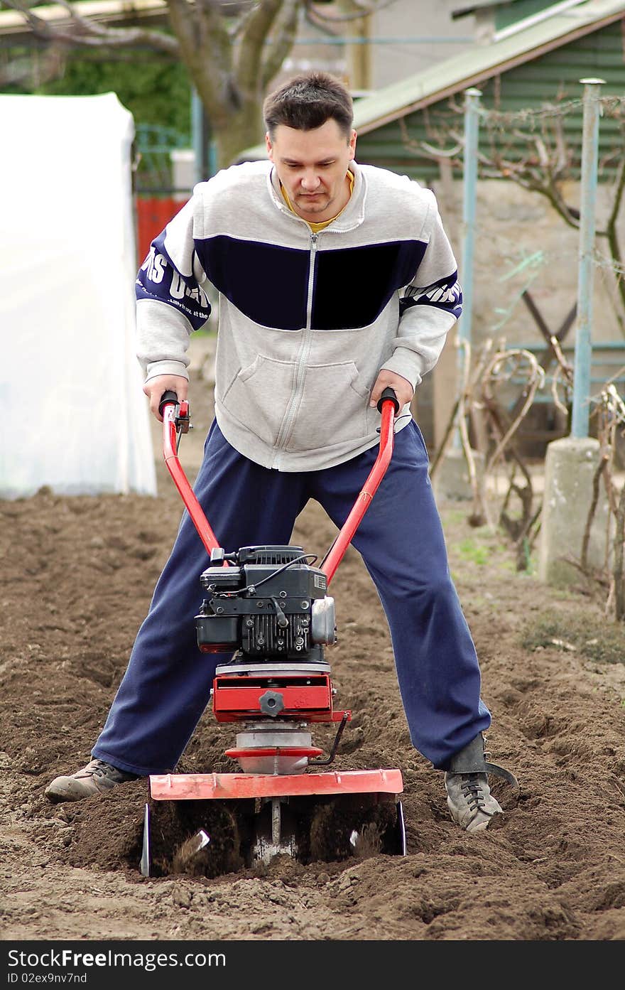 Man rototilling with a red rototiller. Man rototilling with a red rototiller