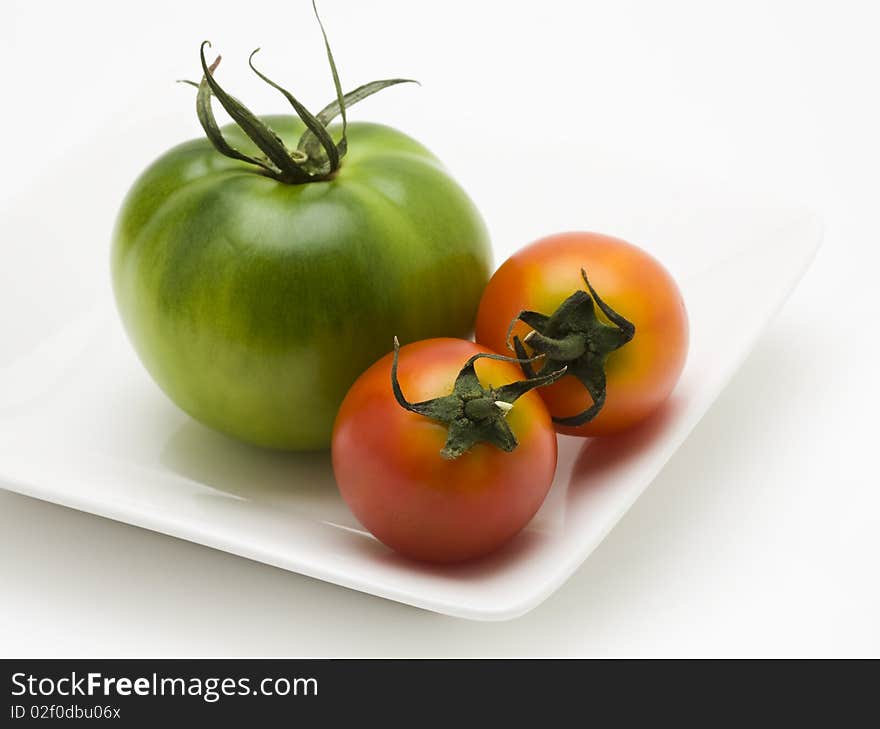 Green and red tomatoes on white plate