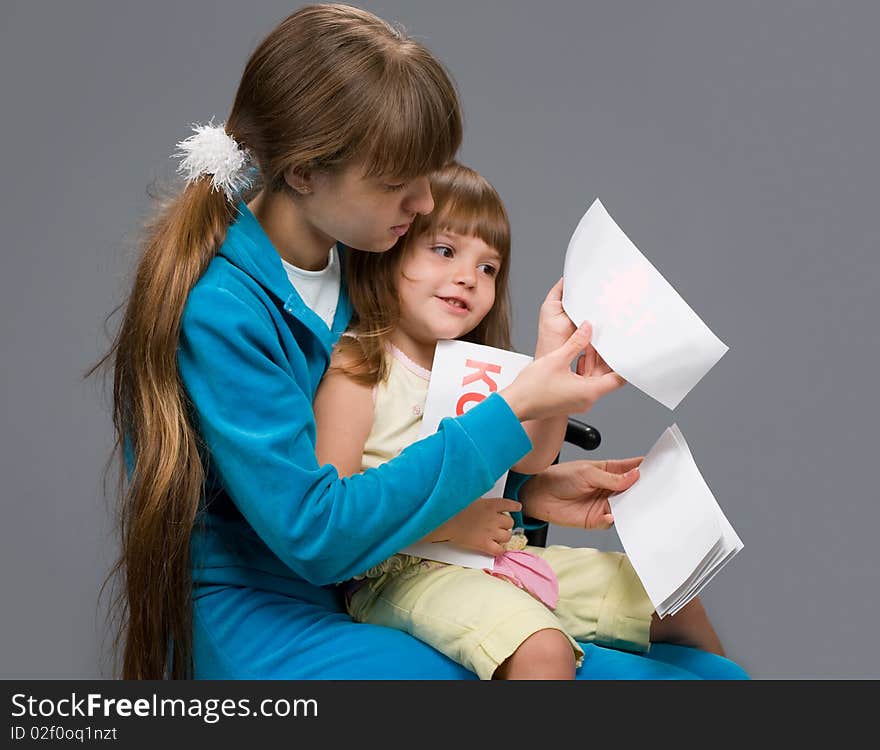 A young girl in a blue suit sitting with a child in her arms and teaches her to read. A young girl in a blue suit sitting with a child in her arms and teaches her to read