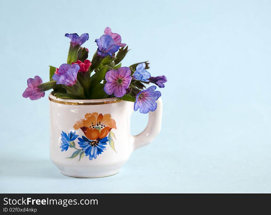 Small bouquet of blue lungwort  (pulmonaria obscura) in a painted cup vase. Small bouquet of blue lungwort  (pulmonaria obscura) in a painted cup vase.