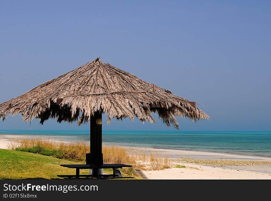 An inviting thatched umbrella on a beautiful tropical beach on the Arabian Gulf.