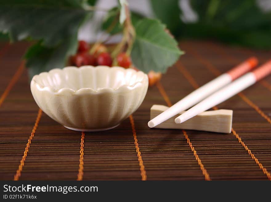 Cup and chopsticks on a wooden napkin against plants. Cup and chopsticks on a wooden napkin against plants