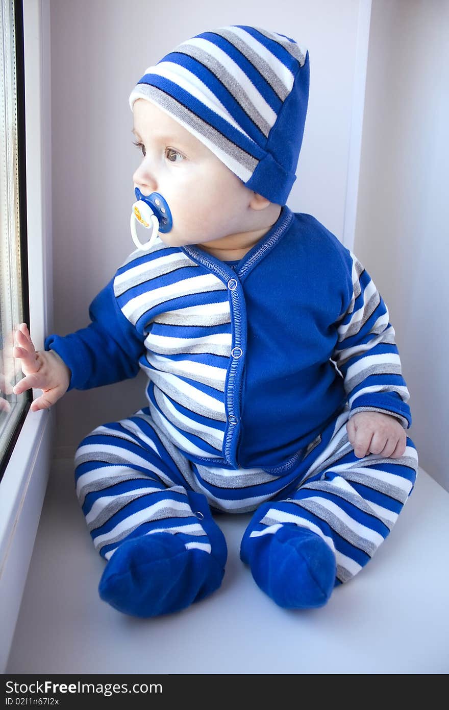 The baby of 6-7 months in a suit in a strip sits and looks out of the window